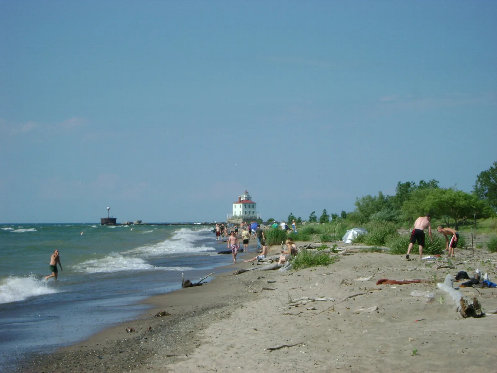 Sandy Lake Erie beach with waves, people and a lighthouse in the distance