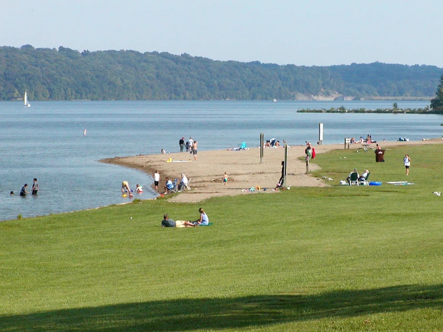 Sandy beach with swimmers on a wide lake and wooded hills across the water