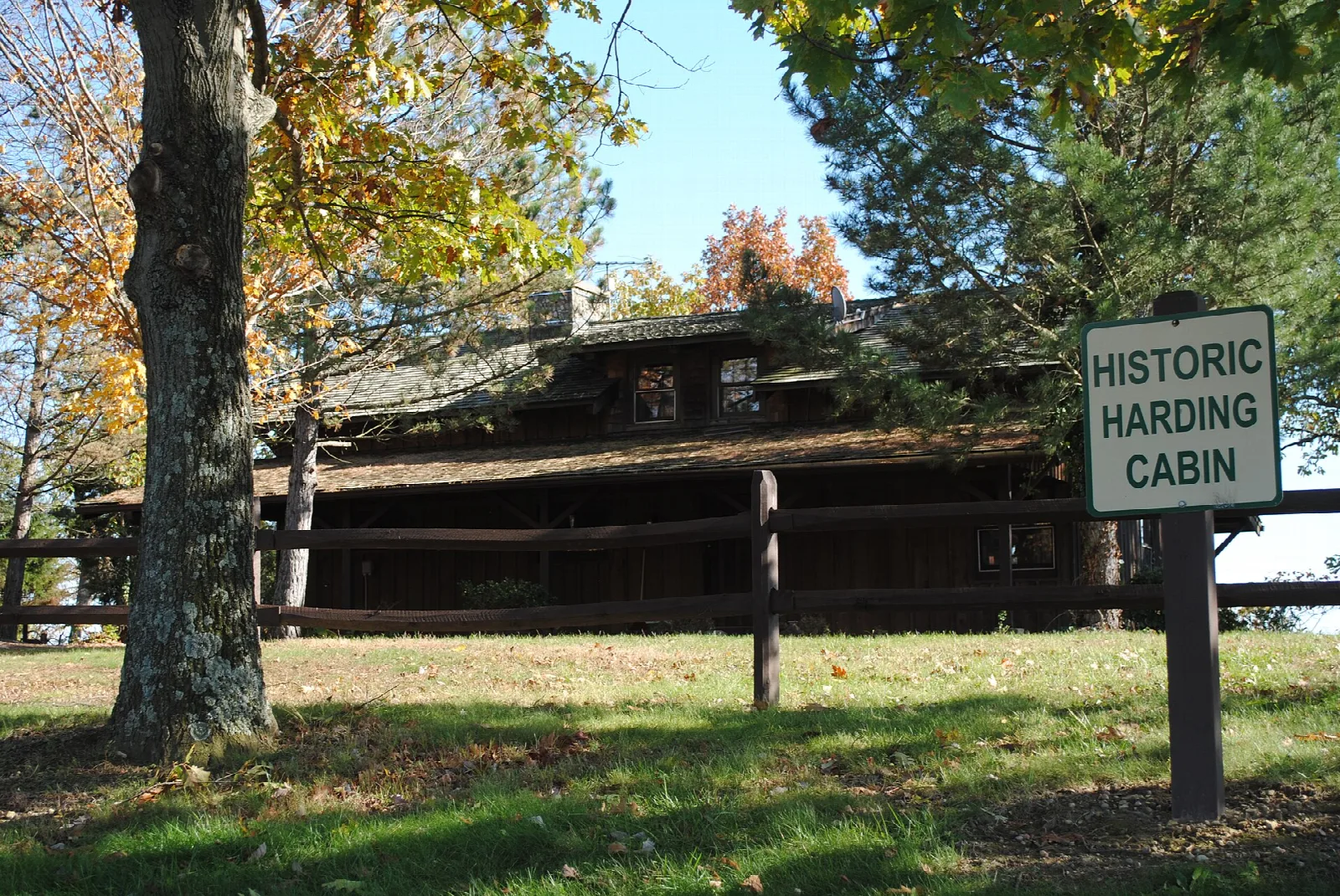 Log cabin behind a split-rail fence and a Historic Harding Cabin sign