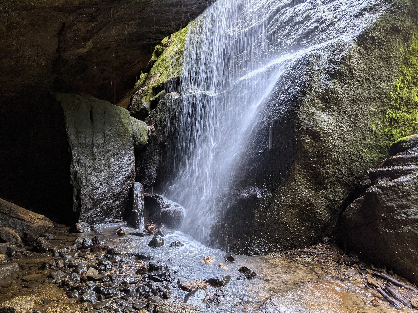 Water spilling down a mossy rock face beside a dark overhang