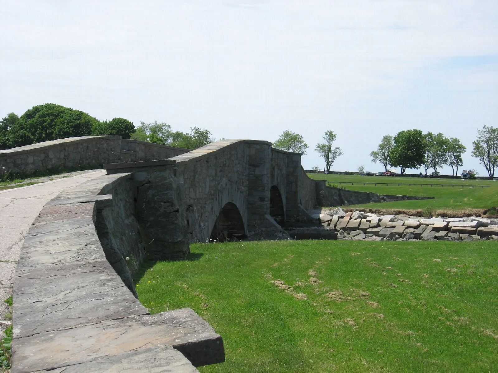 Low stone arch bridge beside a green lawn