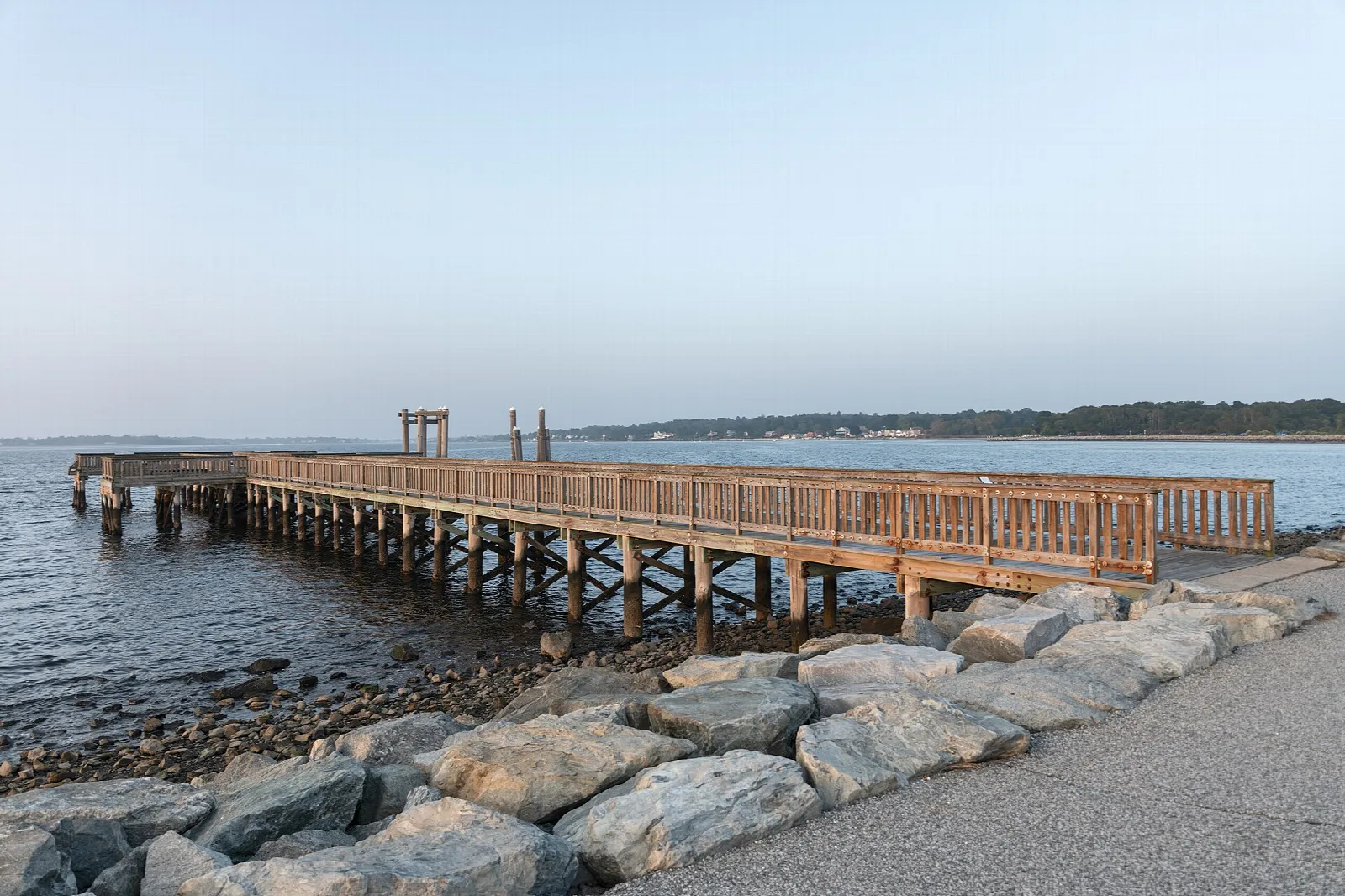 Wooden fishing pier extending over water past a rock-lined shore