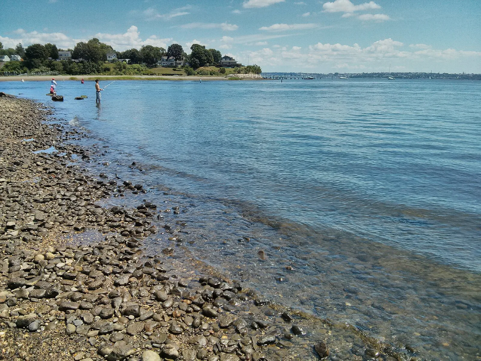 Rocky shoreline with shallow blue water and a tree-lined point in the distance