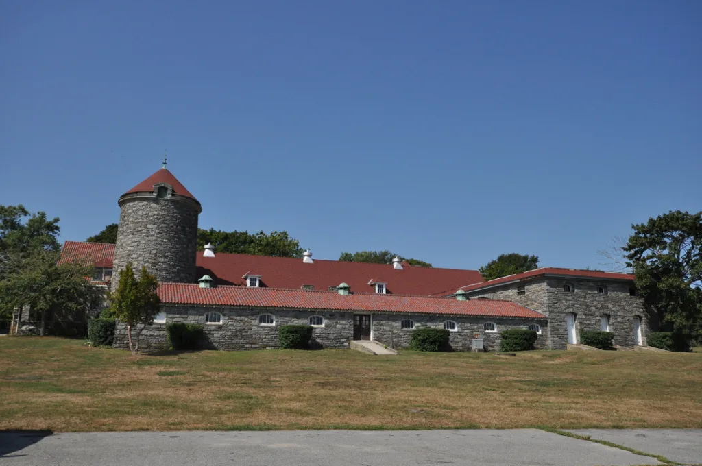 Stone building with a round tower and red roof beside a grass lawn