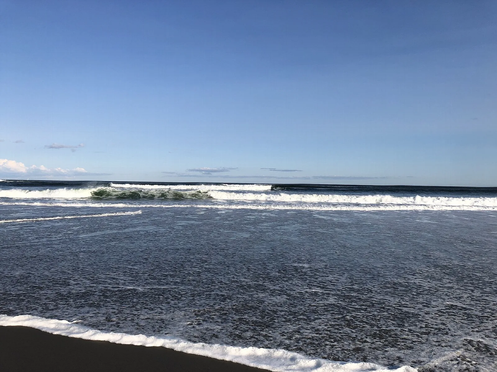Waves rolling onto a dark sand beach under a blue sky