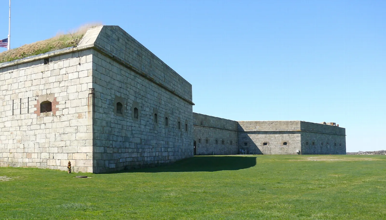 Massive granite fort wall with a grass-topped roof over a green lawn
