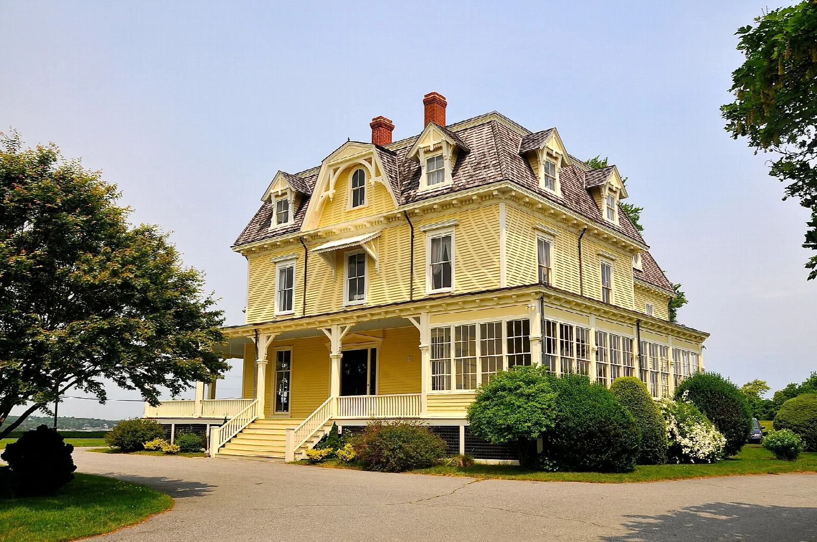 Yellow Victorian house with a wraparound porch and shrubs