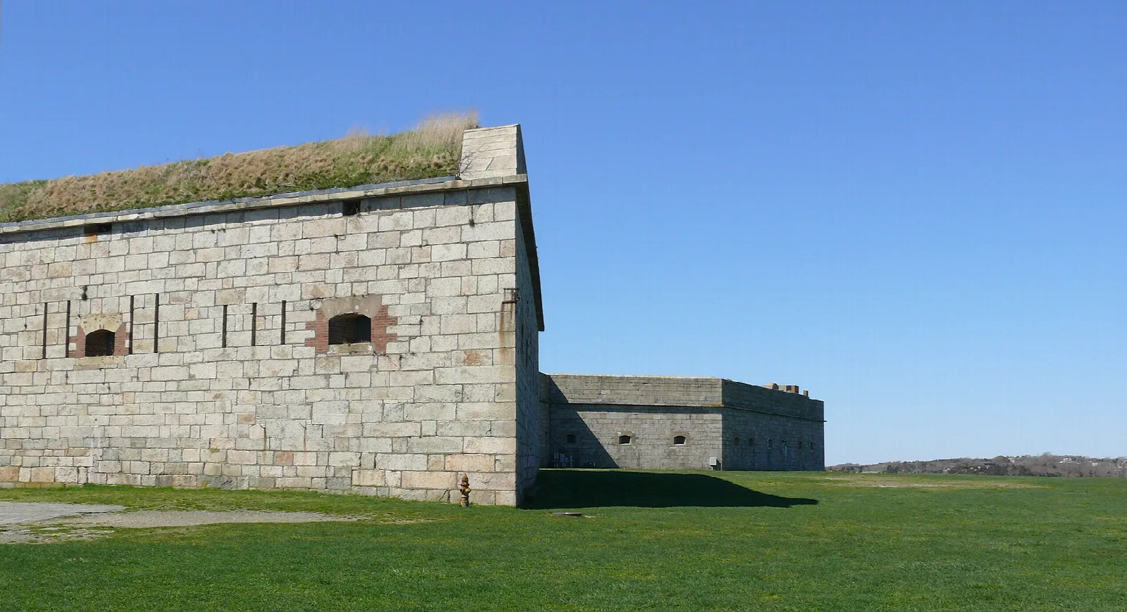 Granite fort wall with embrasures and a grassy roof under a blue sky