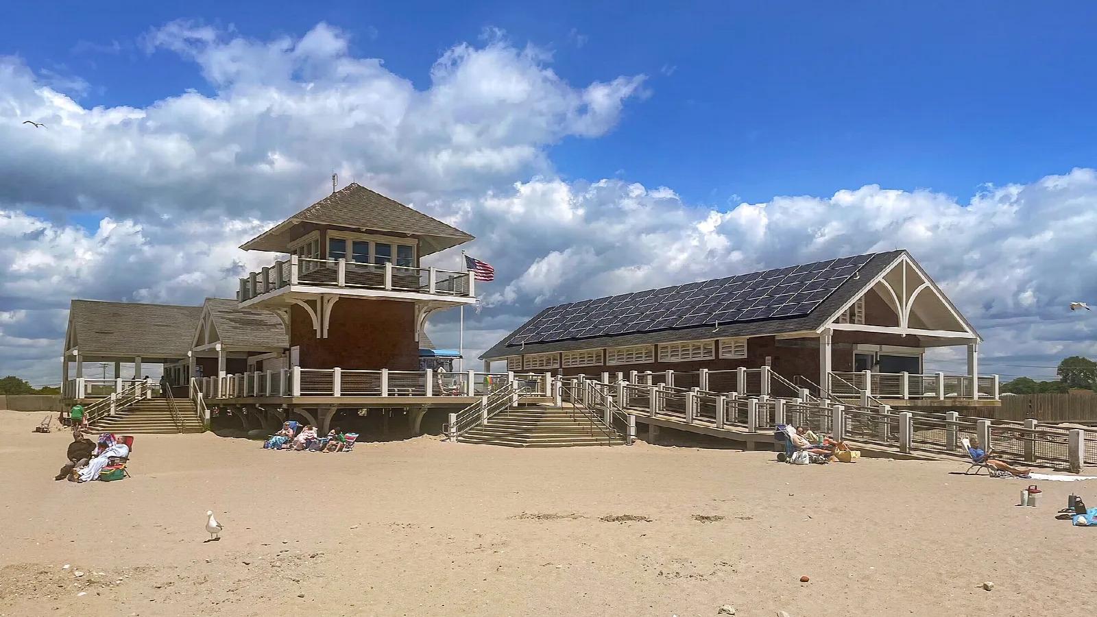 Sandy beach with a wooden pavilion and bath house under a cloudy blue sky