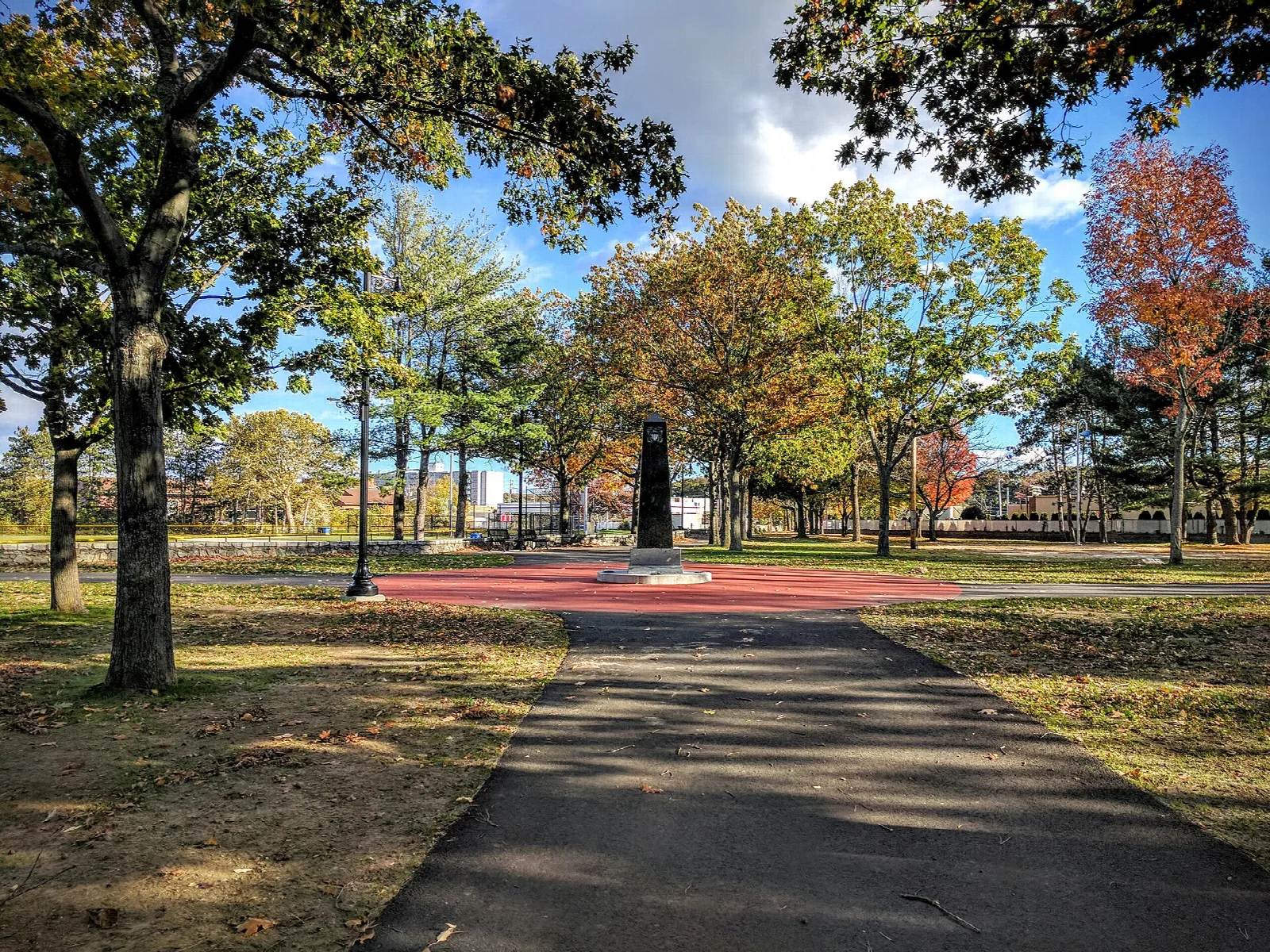 Paved path through a lawn with autumn trees and a red paved plaza