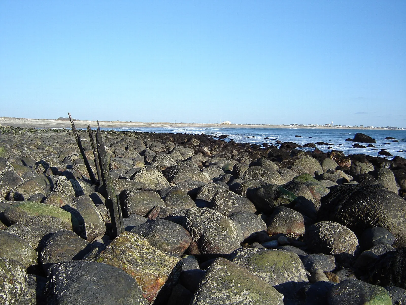 Rounded dark boulders along a shore with the sea and beach beyond