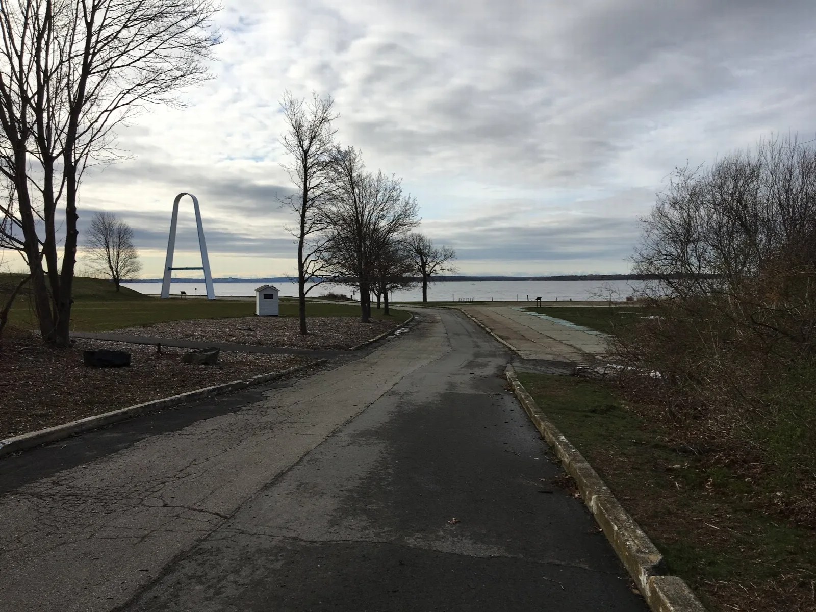 Paved road leading toward a white arch and the water