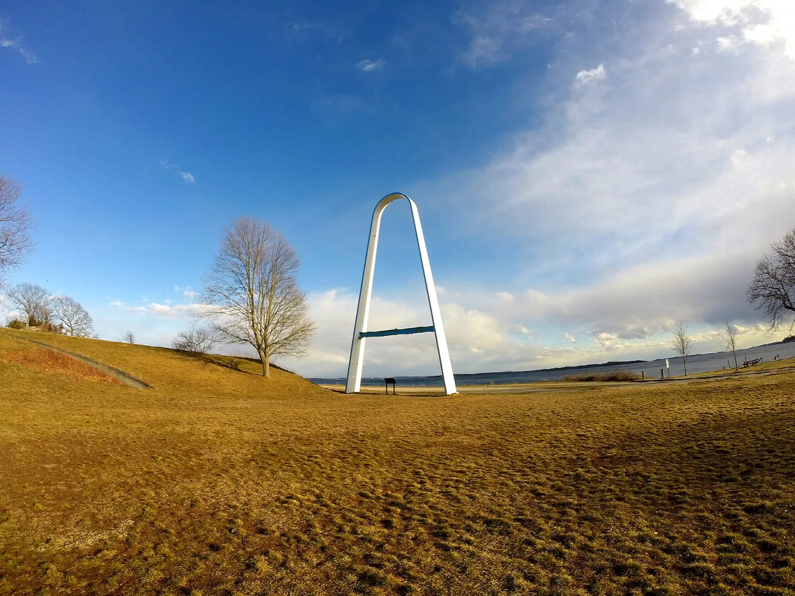 White arch on a golden grass hill under a blue sky with clouds