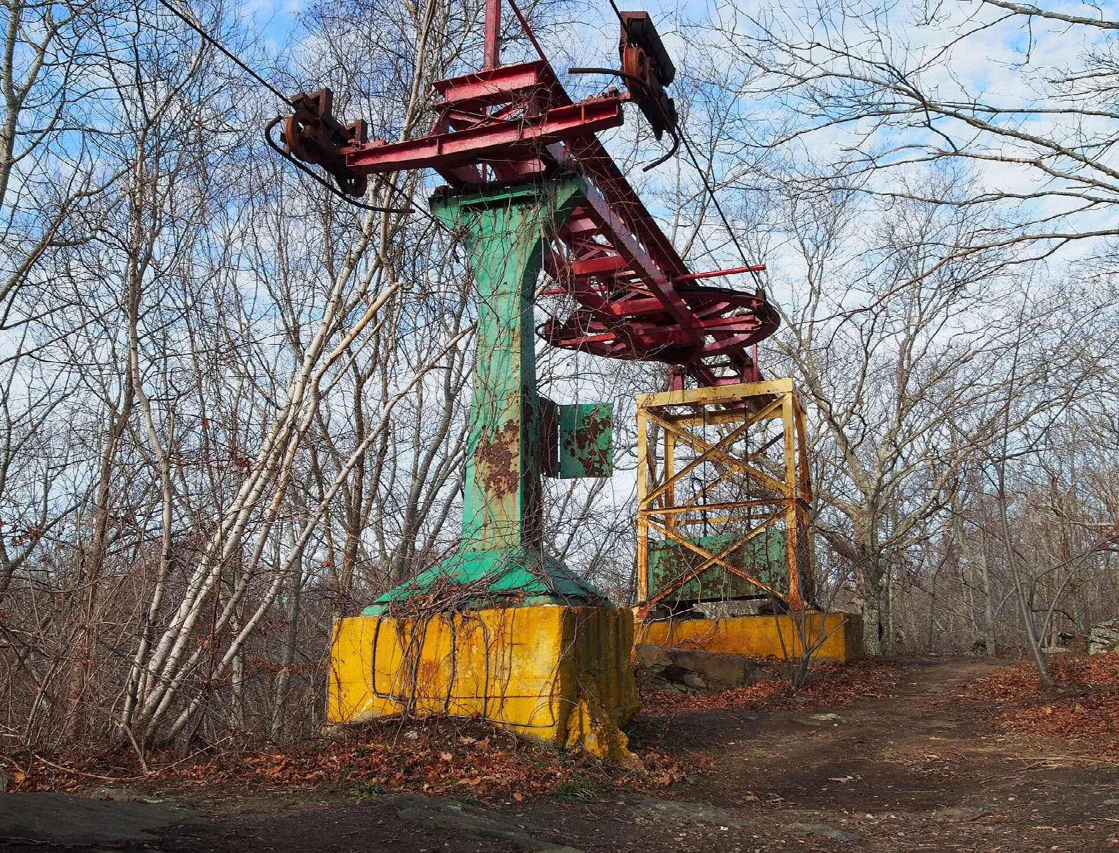Rusted green and red ride tower on yellow footings among bare trees