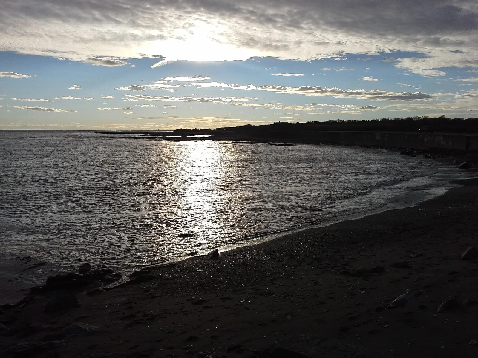 Sun low over a dark sand beach and calm sea with a distant shoreline