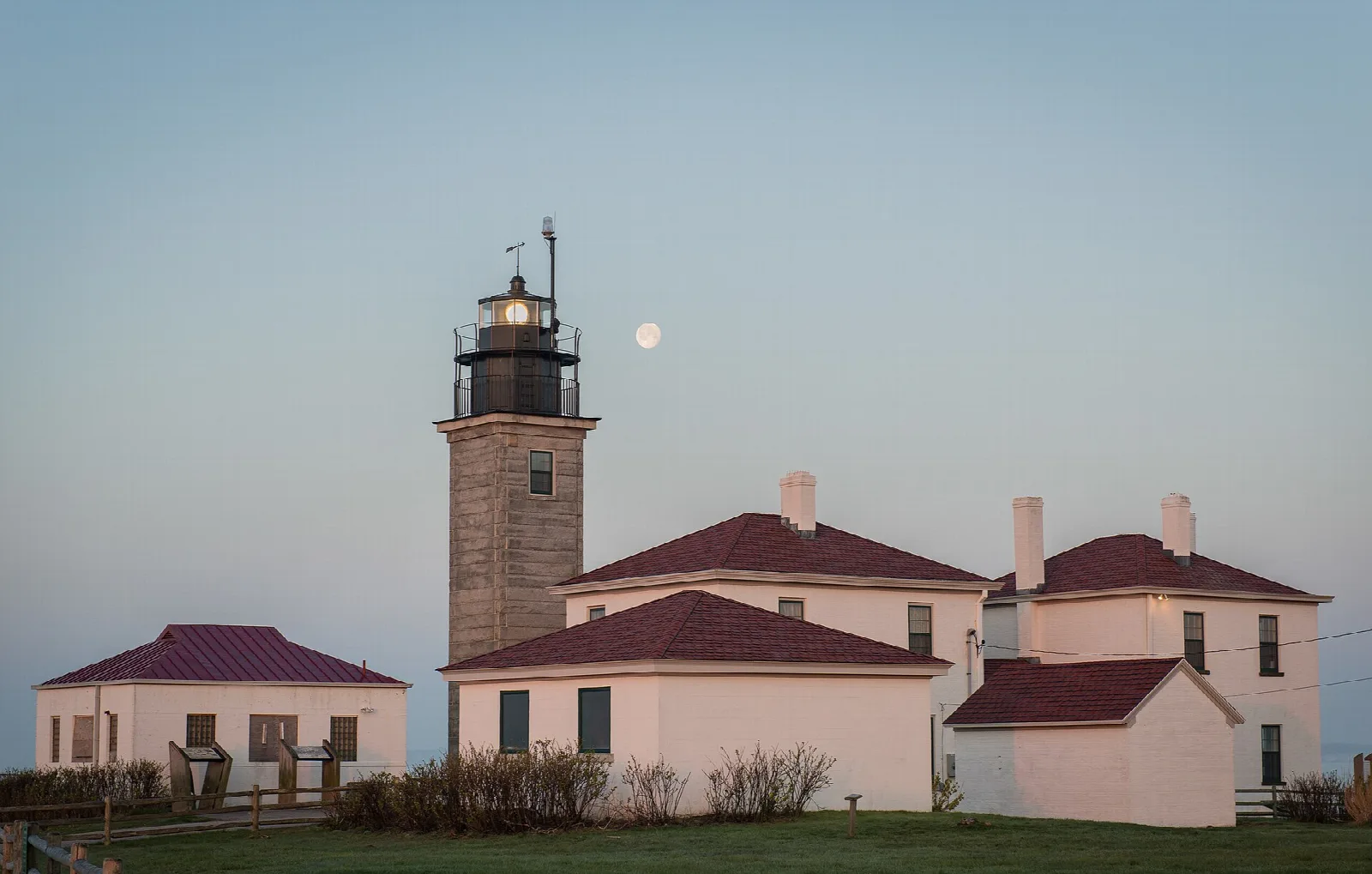 Stone lighthouse tower and pink houses at dusk with the moon above