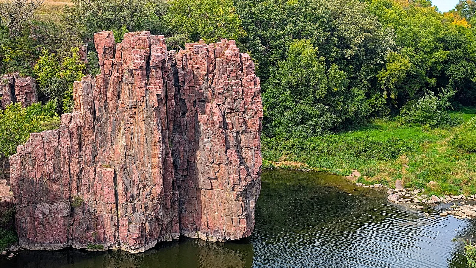 Pink quartzite pillar beside green trees and still water