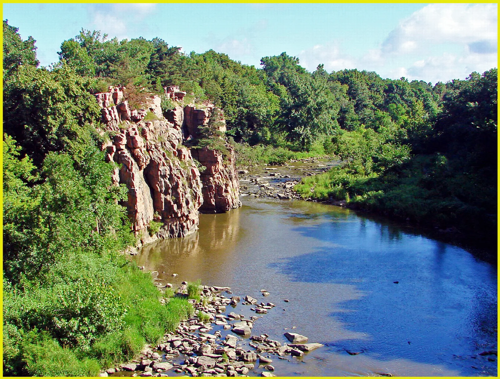 Pink rock outcrop beside a shallow rocky creek and green woods