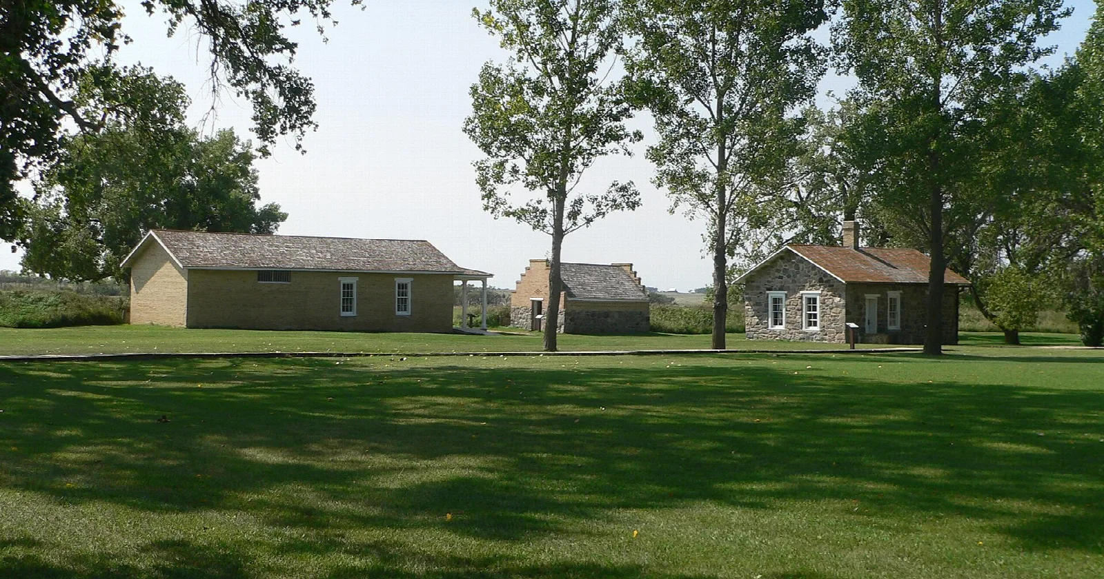 Low stone and brick fort buildings across a mown lawn with trees