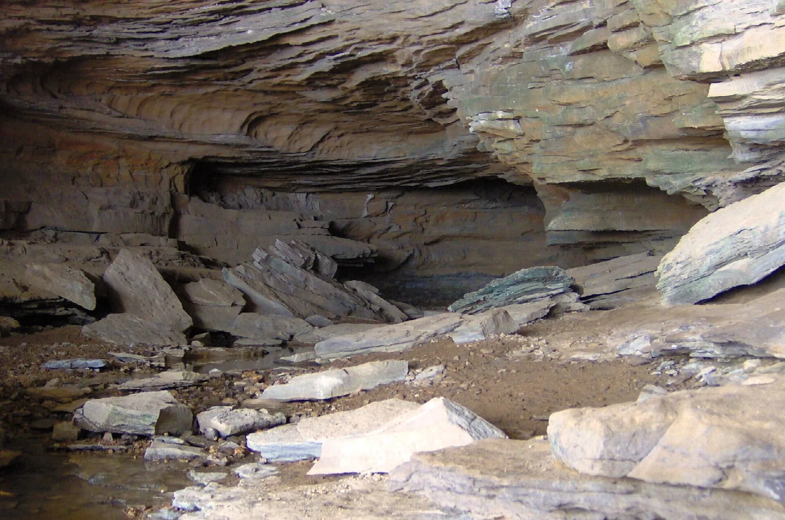Rocky cave mouth with a layered rock overhang and boulders