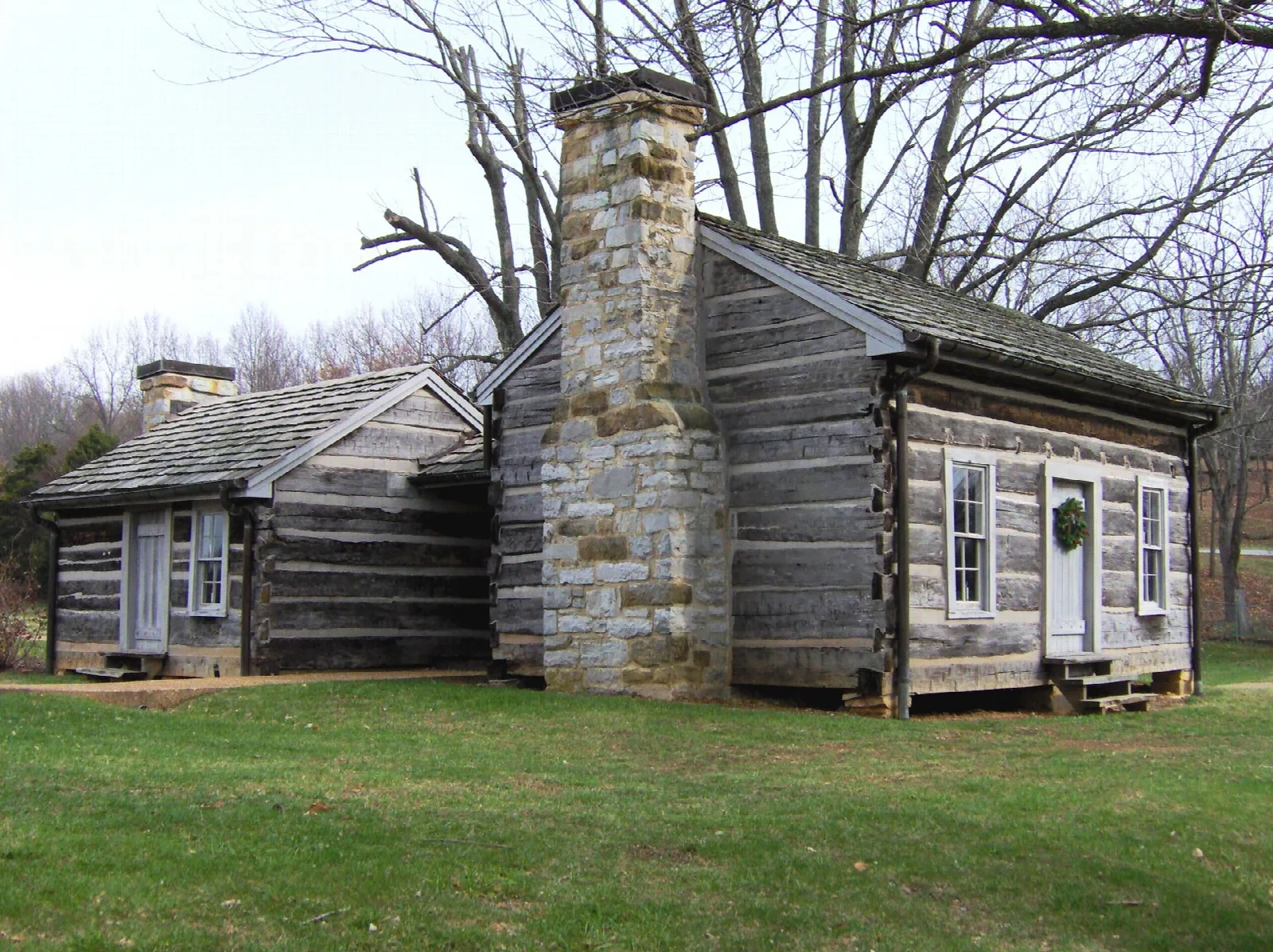 Log cabin with a stone chimney on a grassy lawn