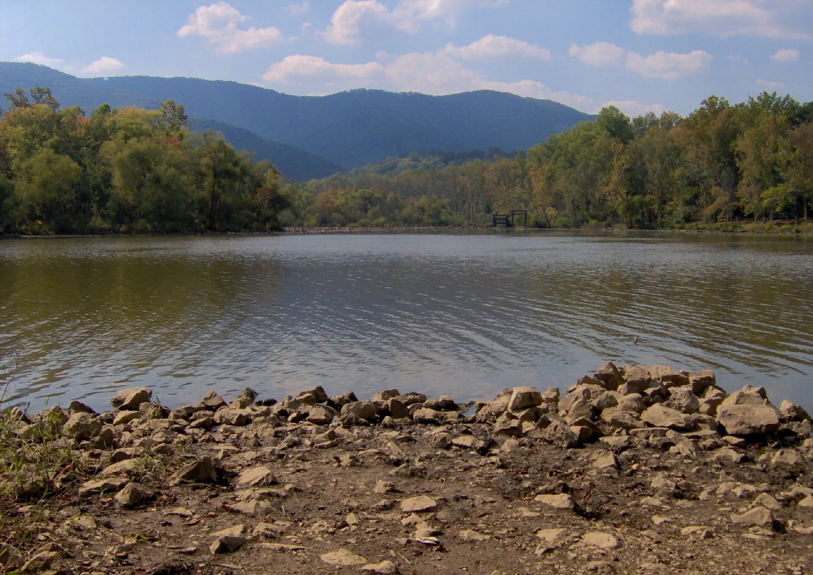 Calm lake with forested hills and mountains behind a rocky shore