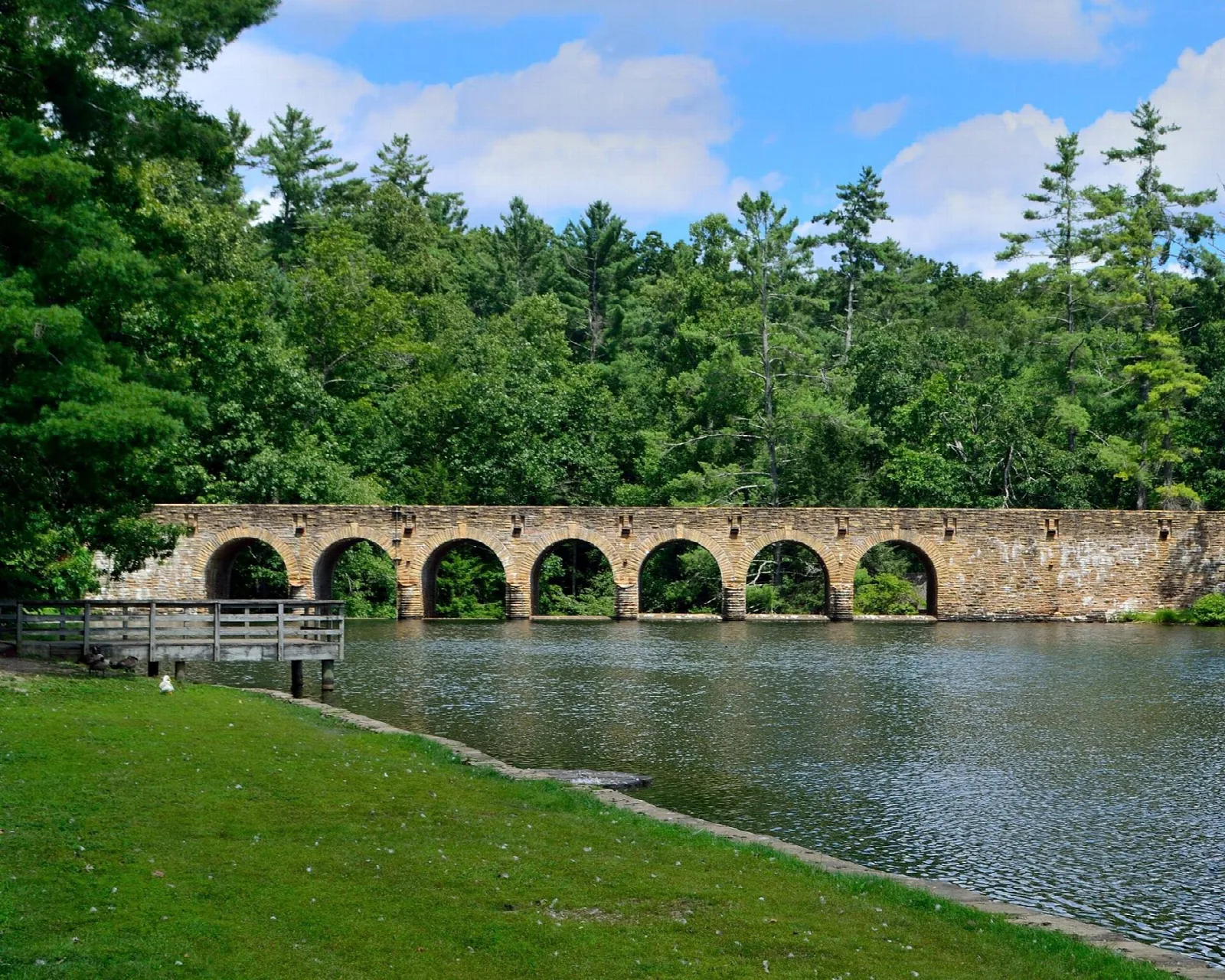 Stone arched dam bridge across a lake with pines behind