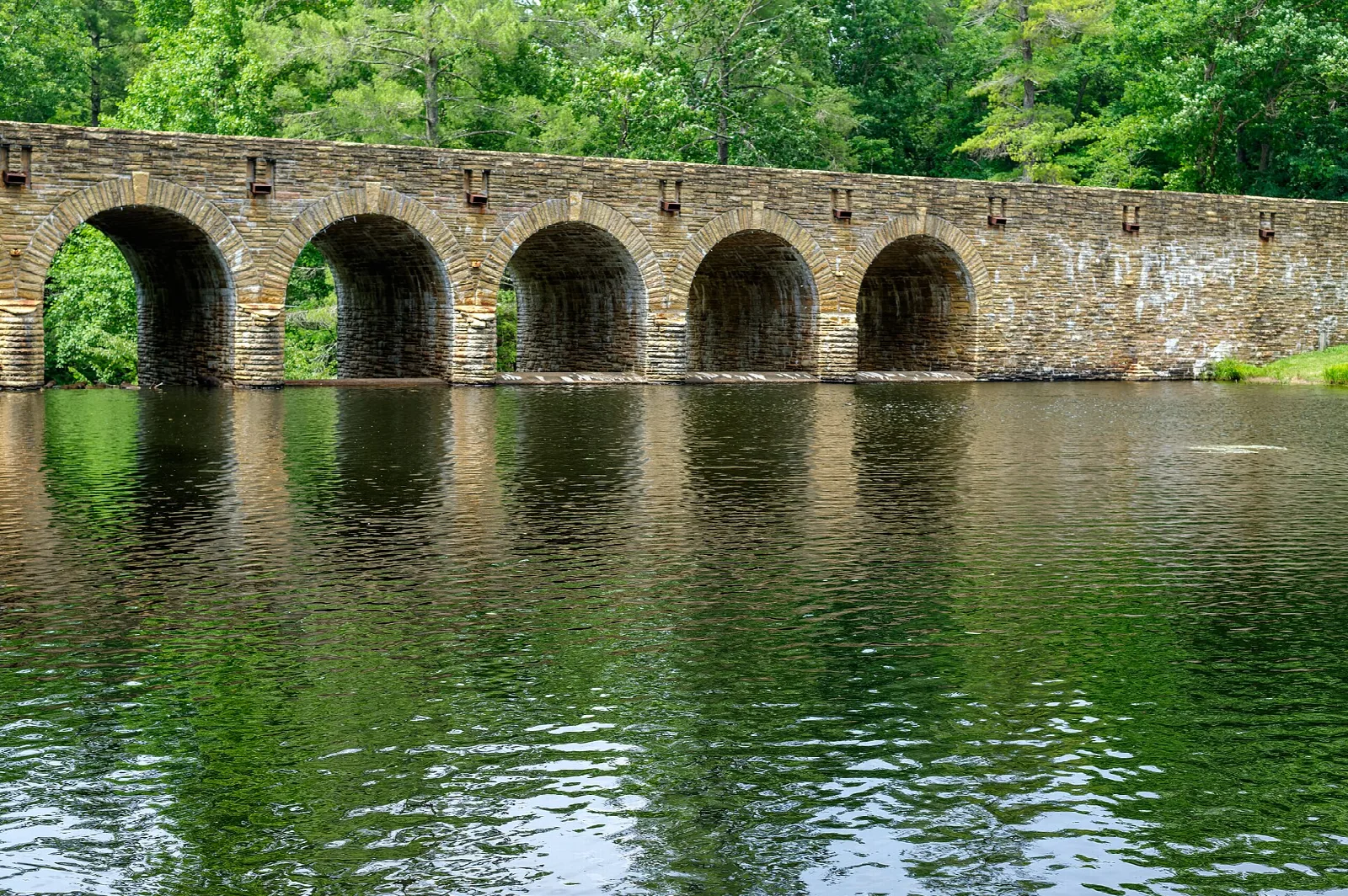 Long stone arched bridge reflected in a calm green lake