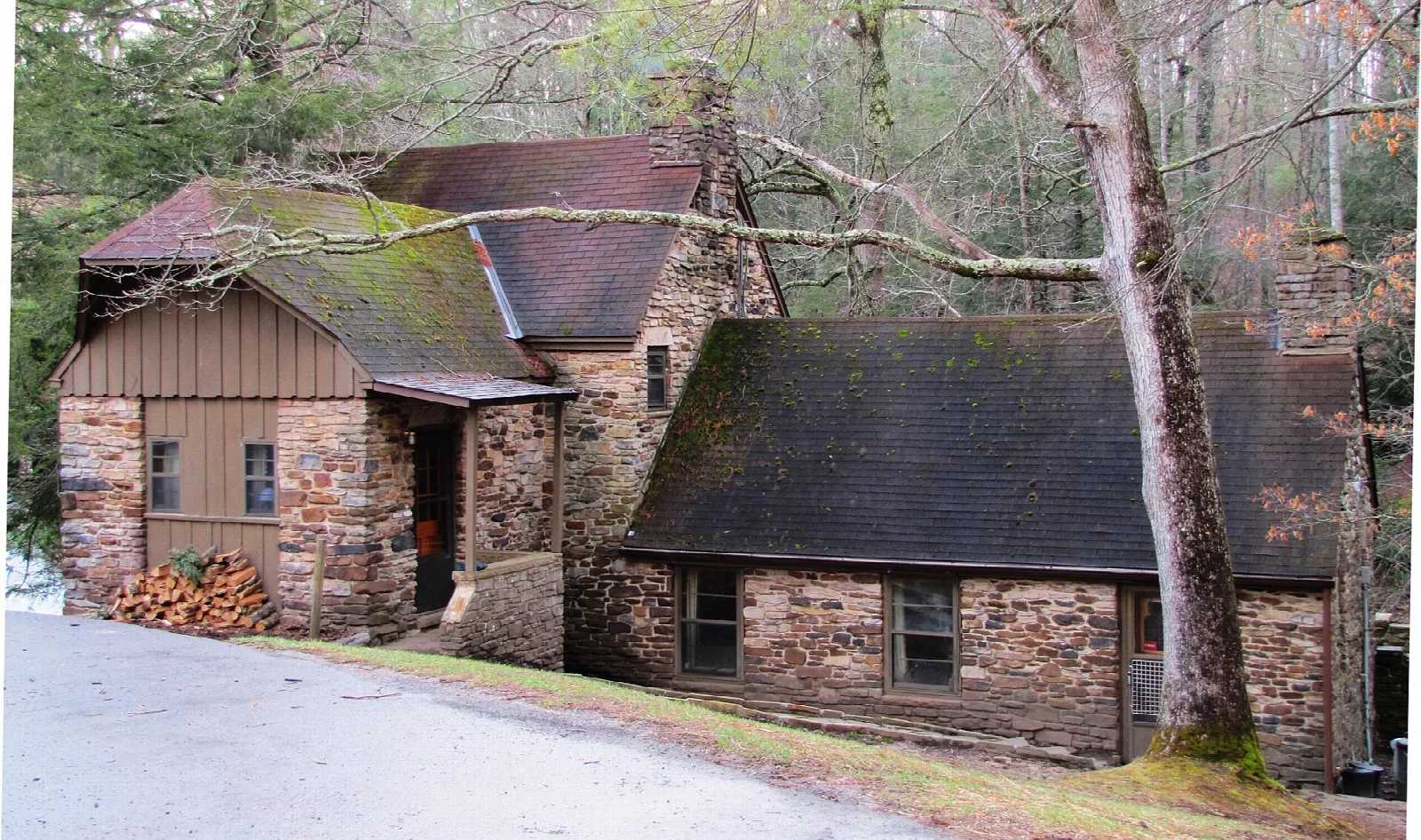 Stone and wood millhouse beside a gravel drive in winter woods