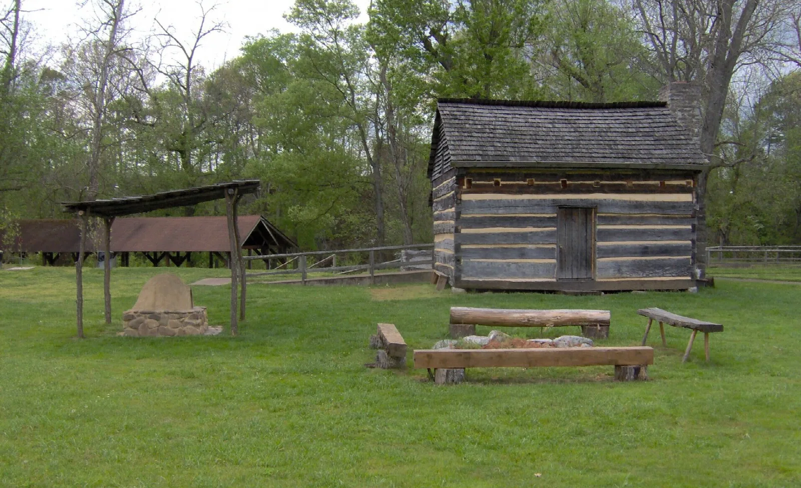 Small log cabin on a lawn with a picnic shelter and benches