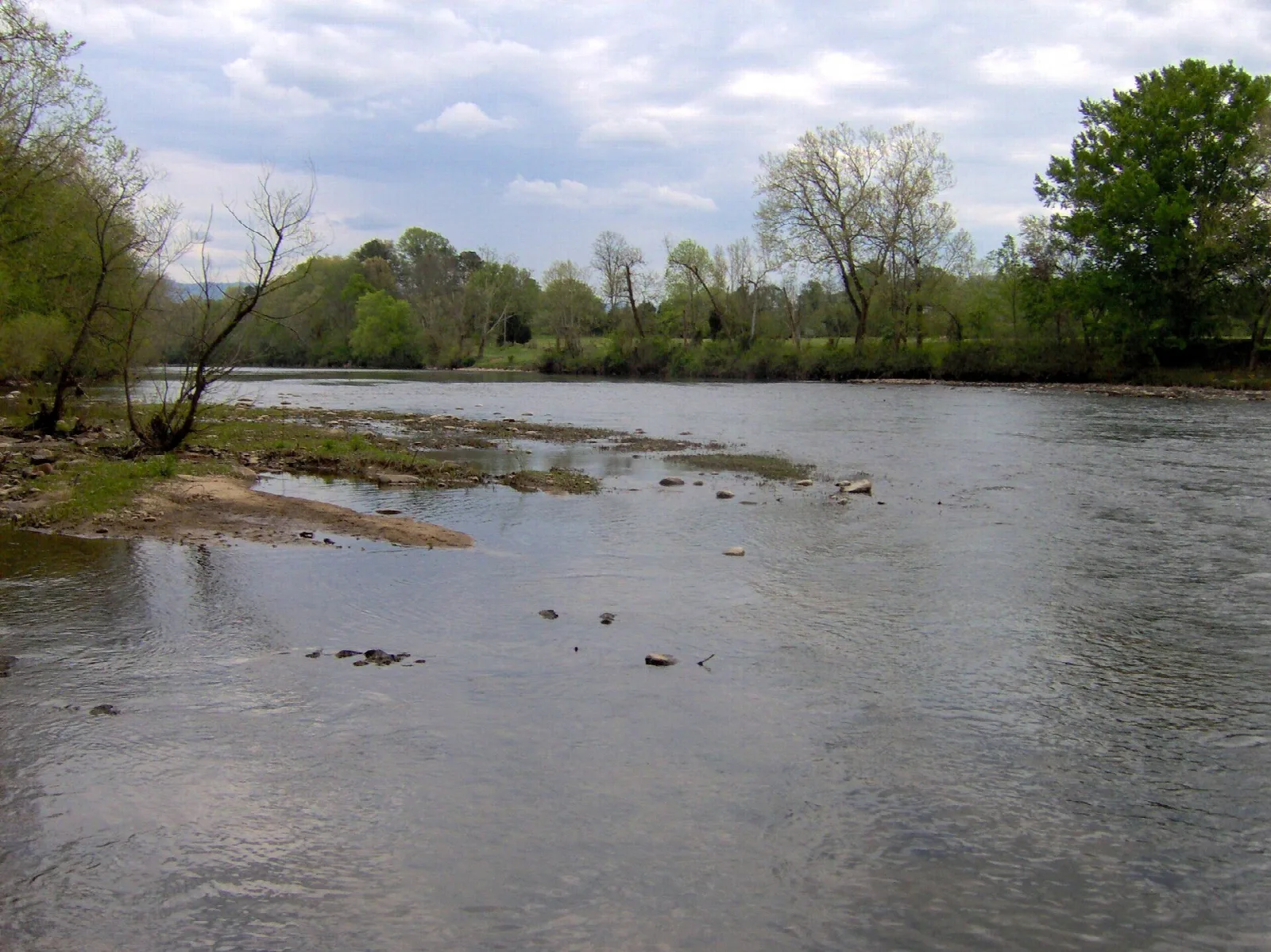 Wide shallow river with tree-lined banks under a cloudy sky