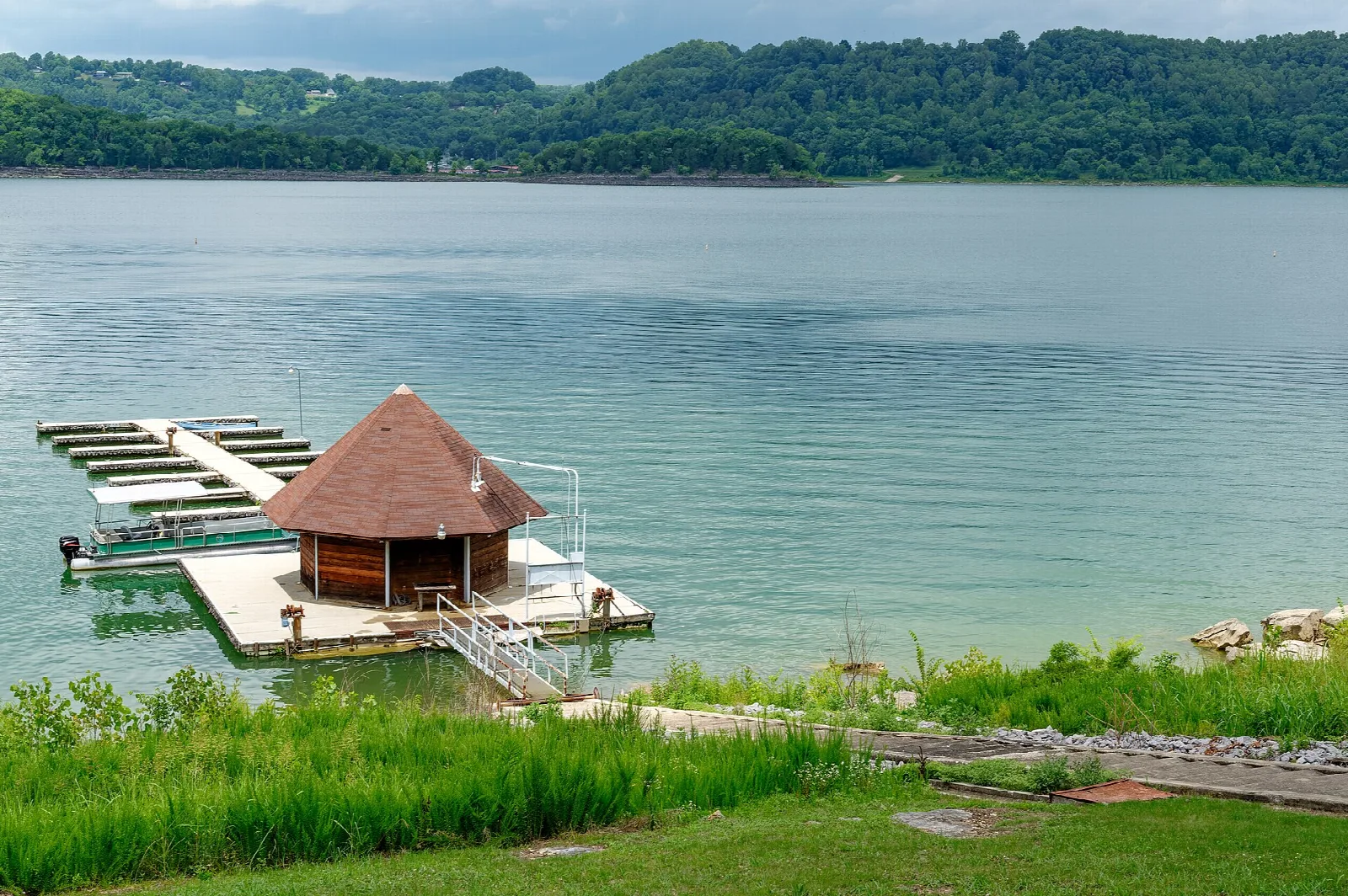 Boat slips and a small roofed dock on a wide green lake with wooded hills
