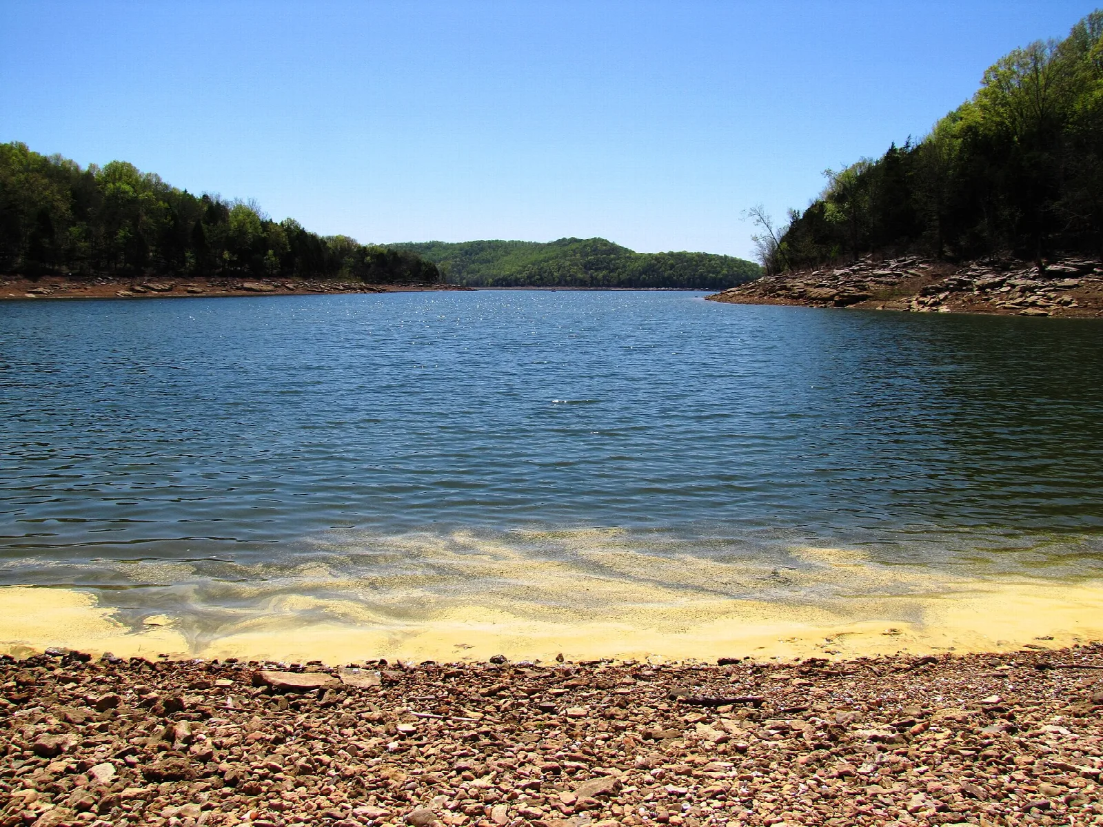 Blue lake with a sandy and gravel shoreline and forested hills
