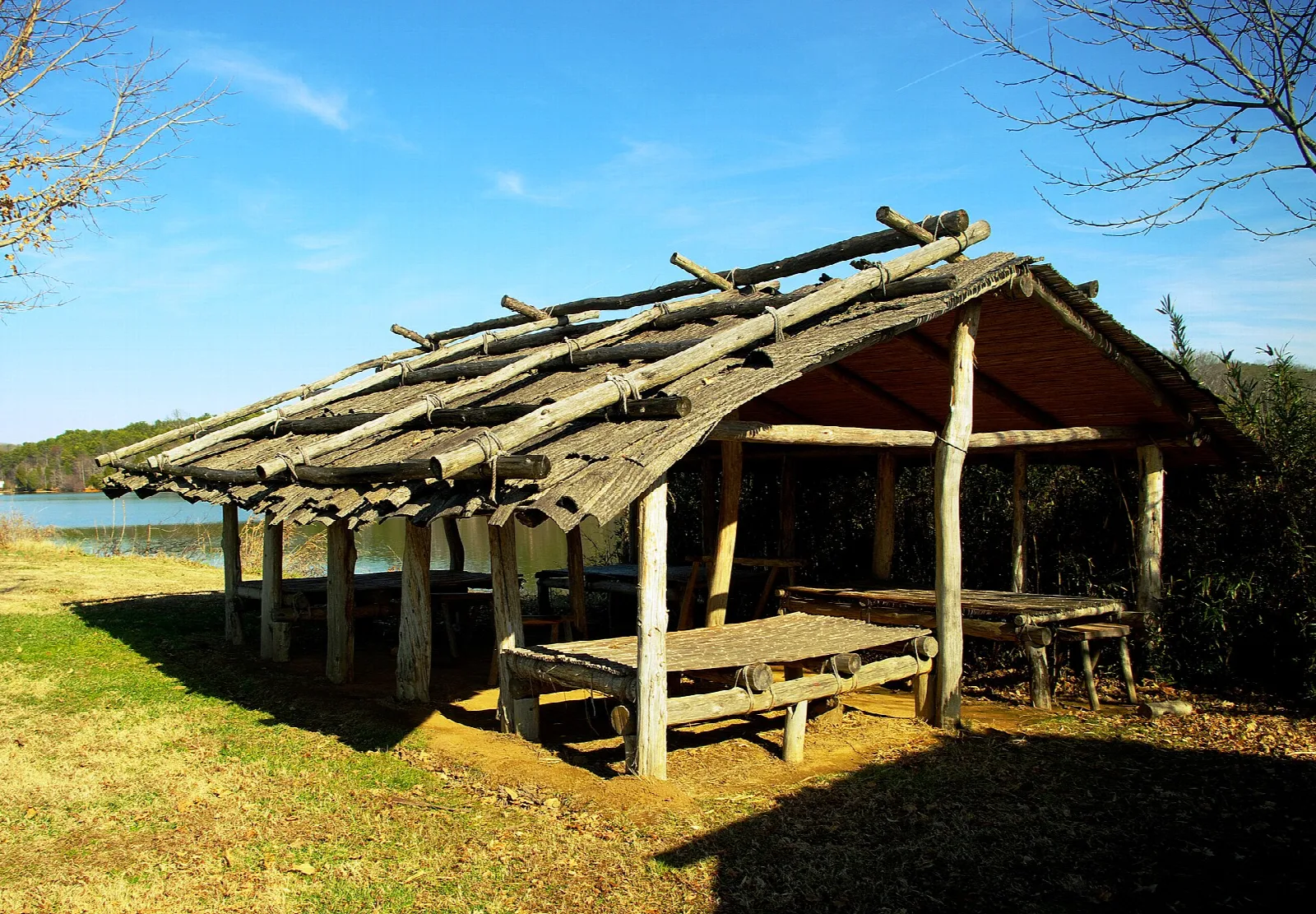 Open-sided thatched shelter with a picnic table beside a lake