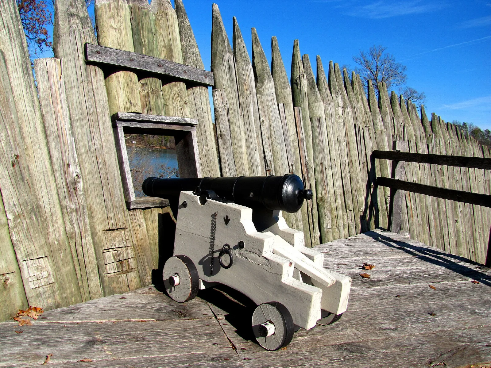 Small black cannon on a wooden platform behind a log wall
