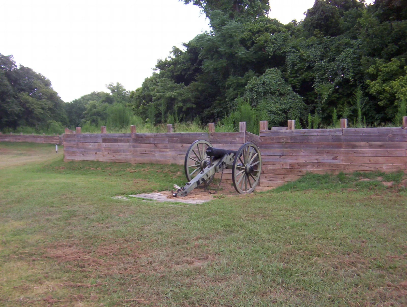 Cannon on grass beside a wooden earthwork wall with trees behind