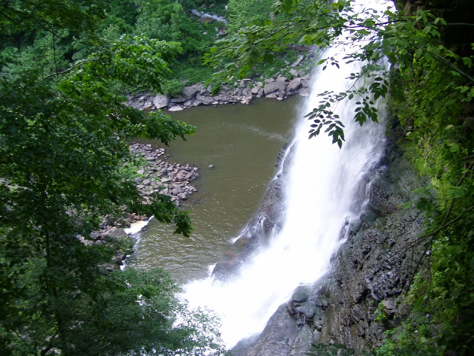 Tall waterfall dropping beside a rocky wall into a green pool
