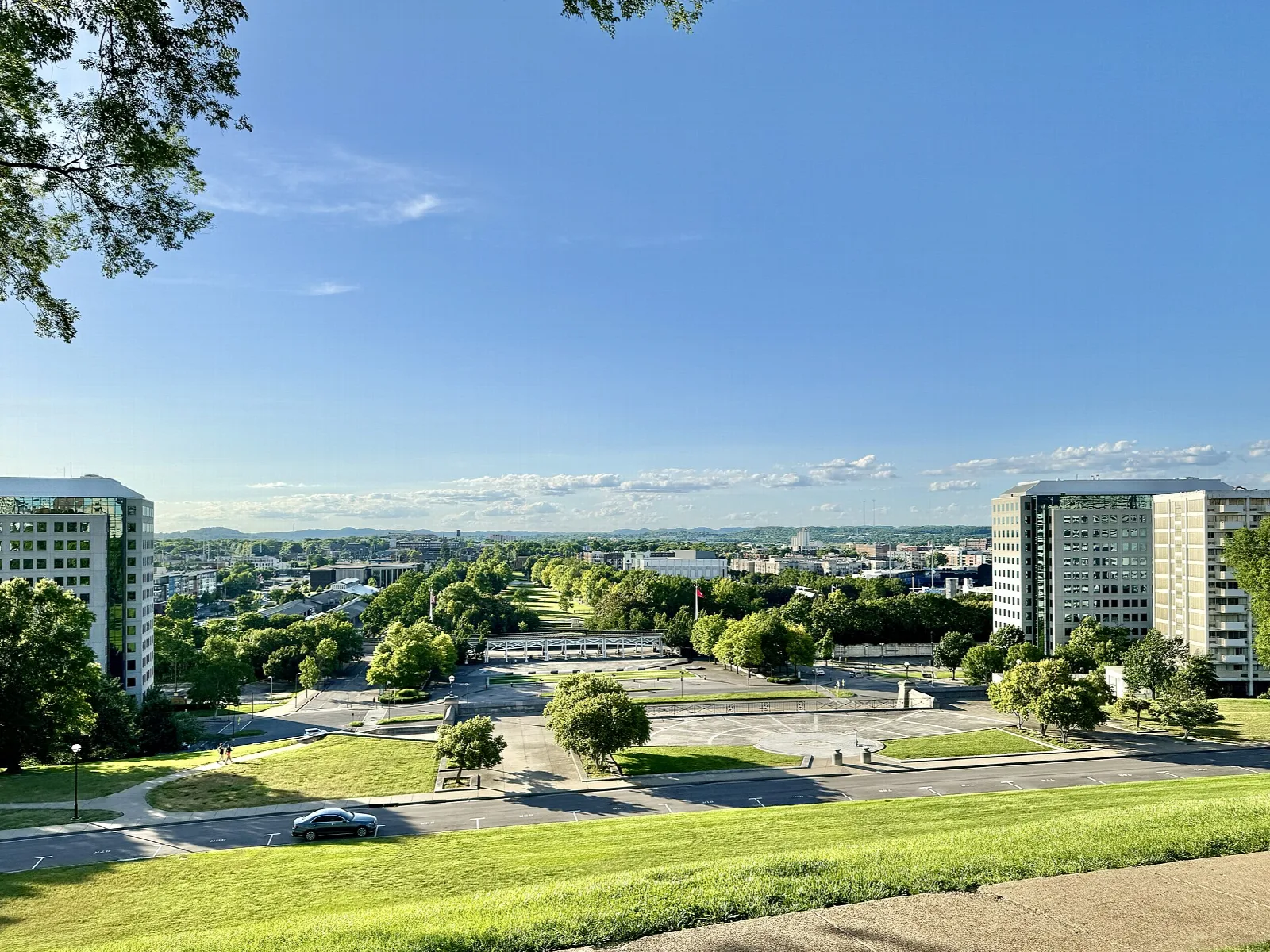 Wide grassy lawn and path in a city park with buildings in the distance