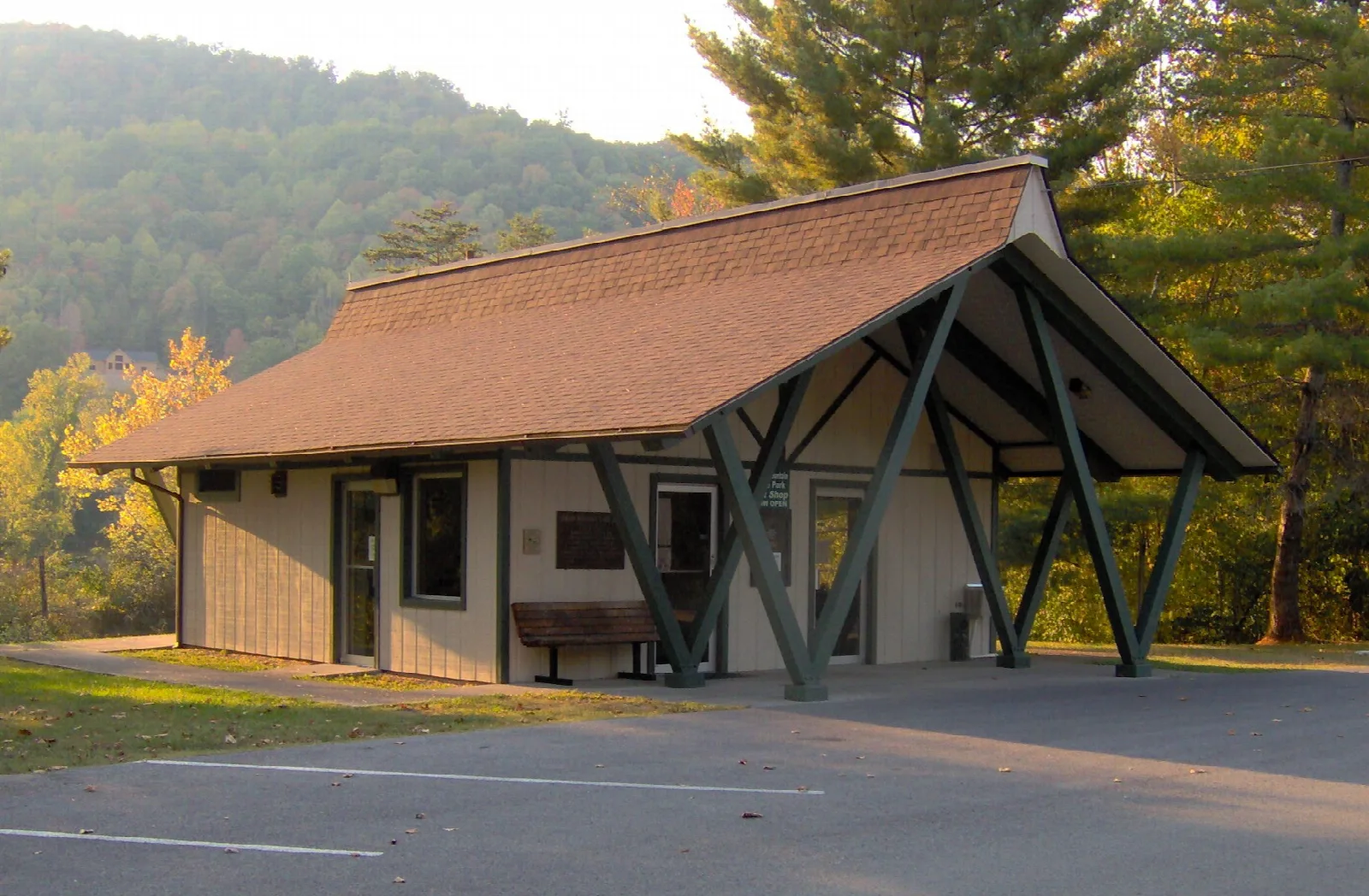 Small wood-roofed building beside a parking area with forested hills behind