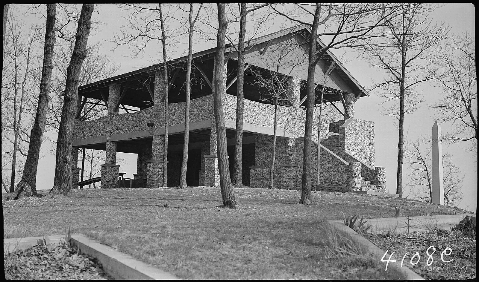 Historic black and white photo of a stone and timber pavilion in bare woods