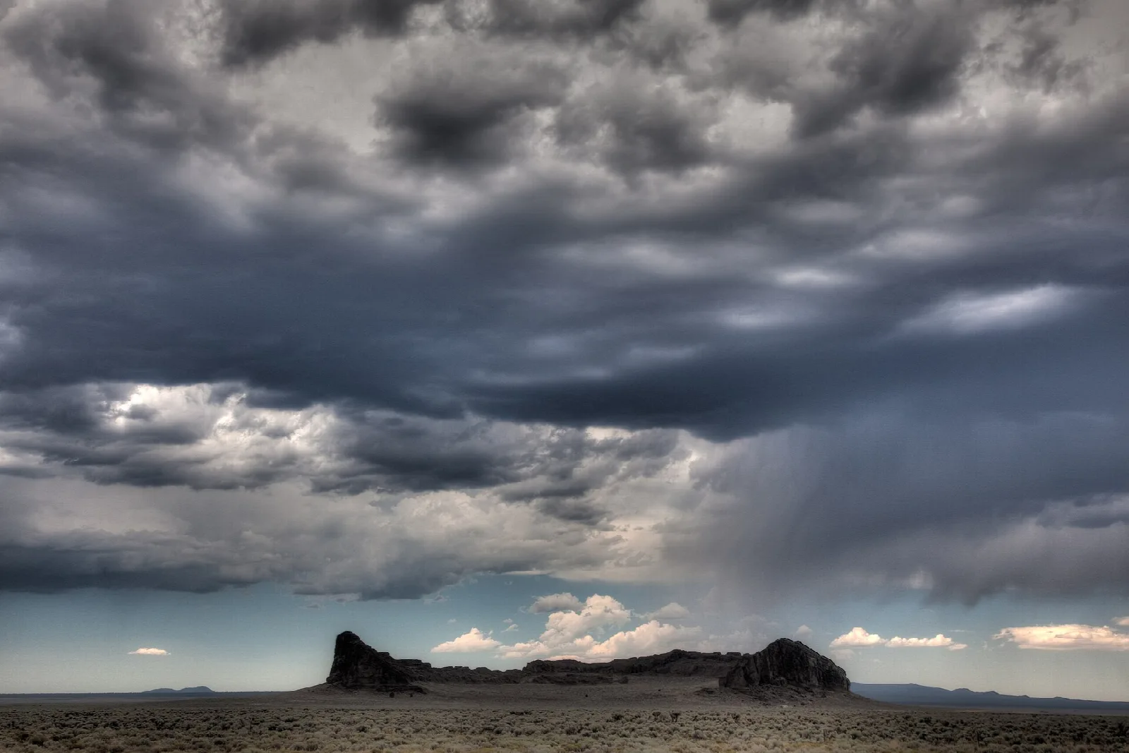 Dark rock formation on a flat desert plain under a storm cloud