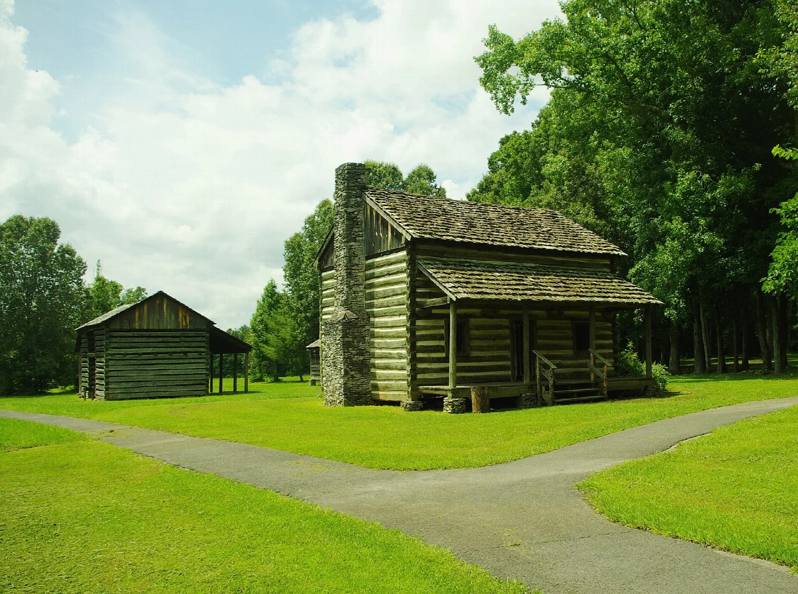 Log cabin and small barn on a green lawn beside a curving path
