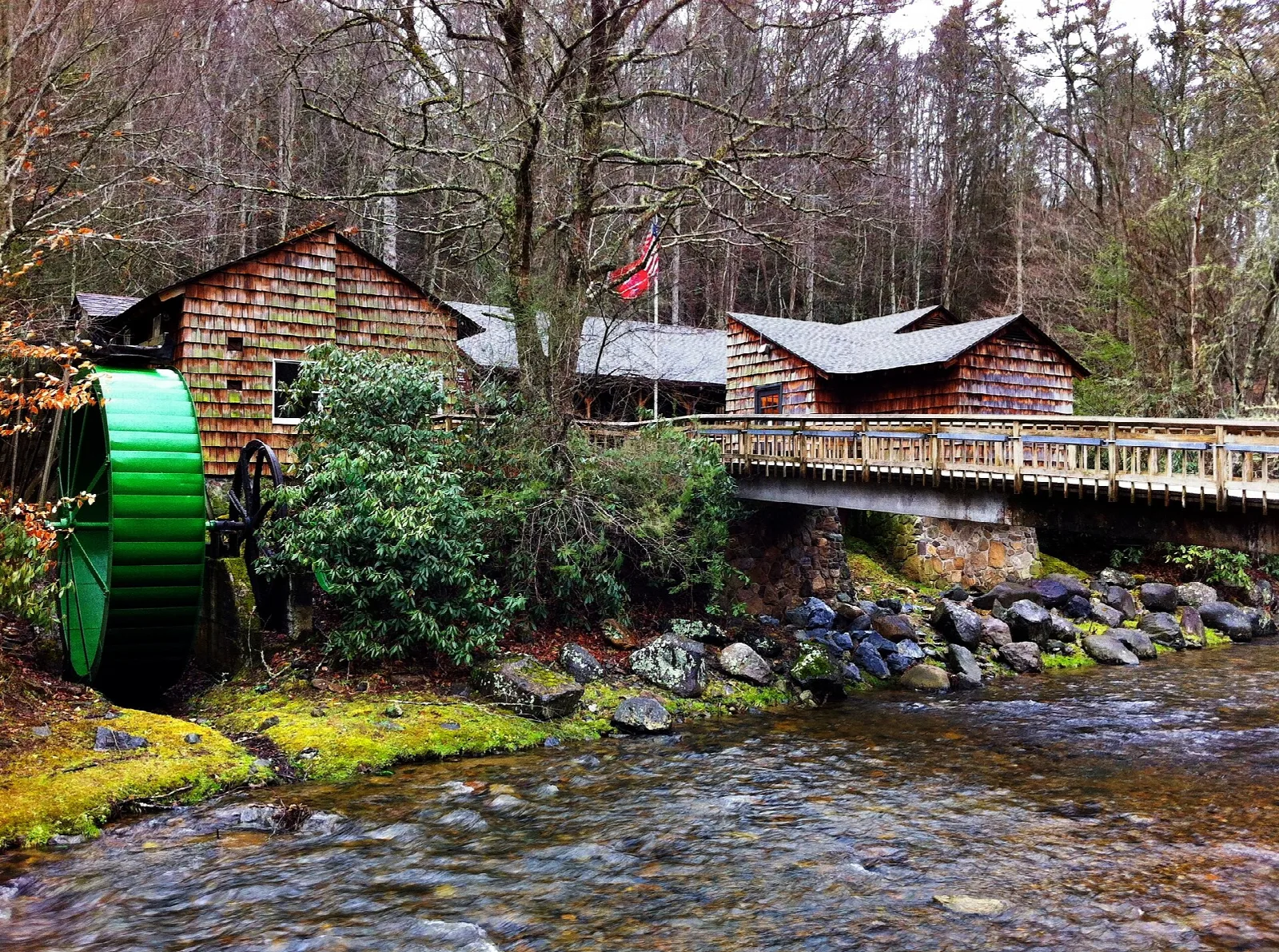 Log mill with a green water wheel beside a rocky creek