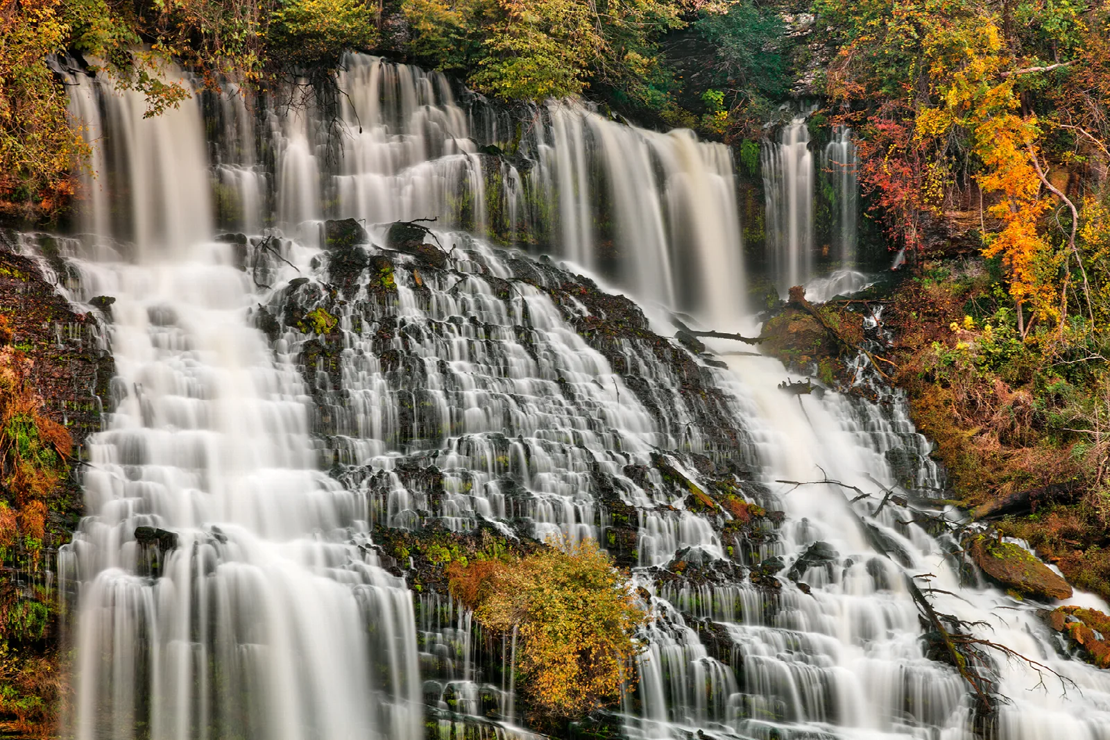 Long-exposure waterfall tumbling over wide rock ledges with fall color
