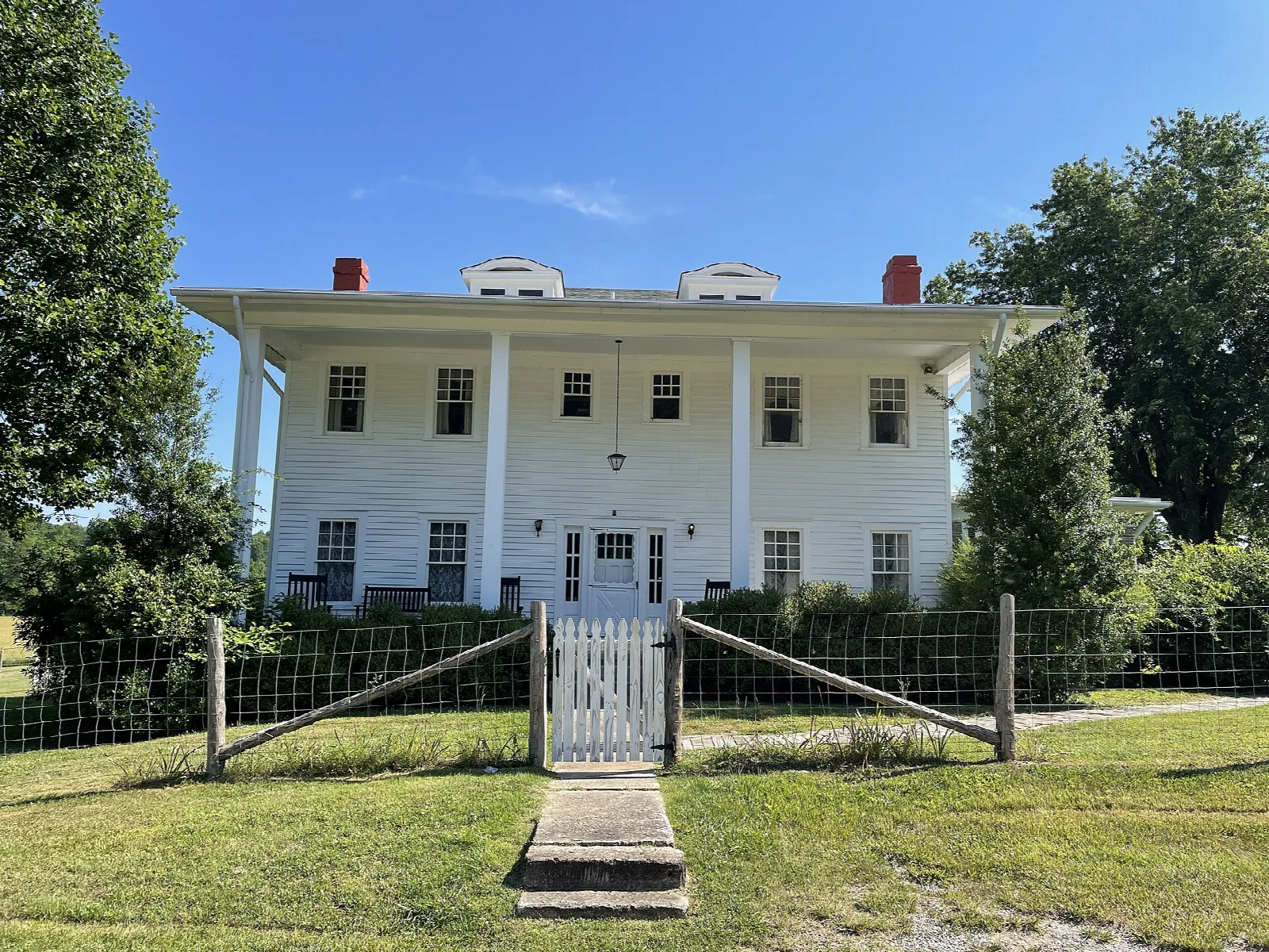 Large white two-story house with columns behind a fence and lawn