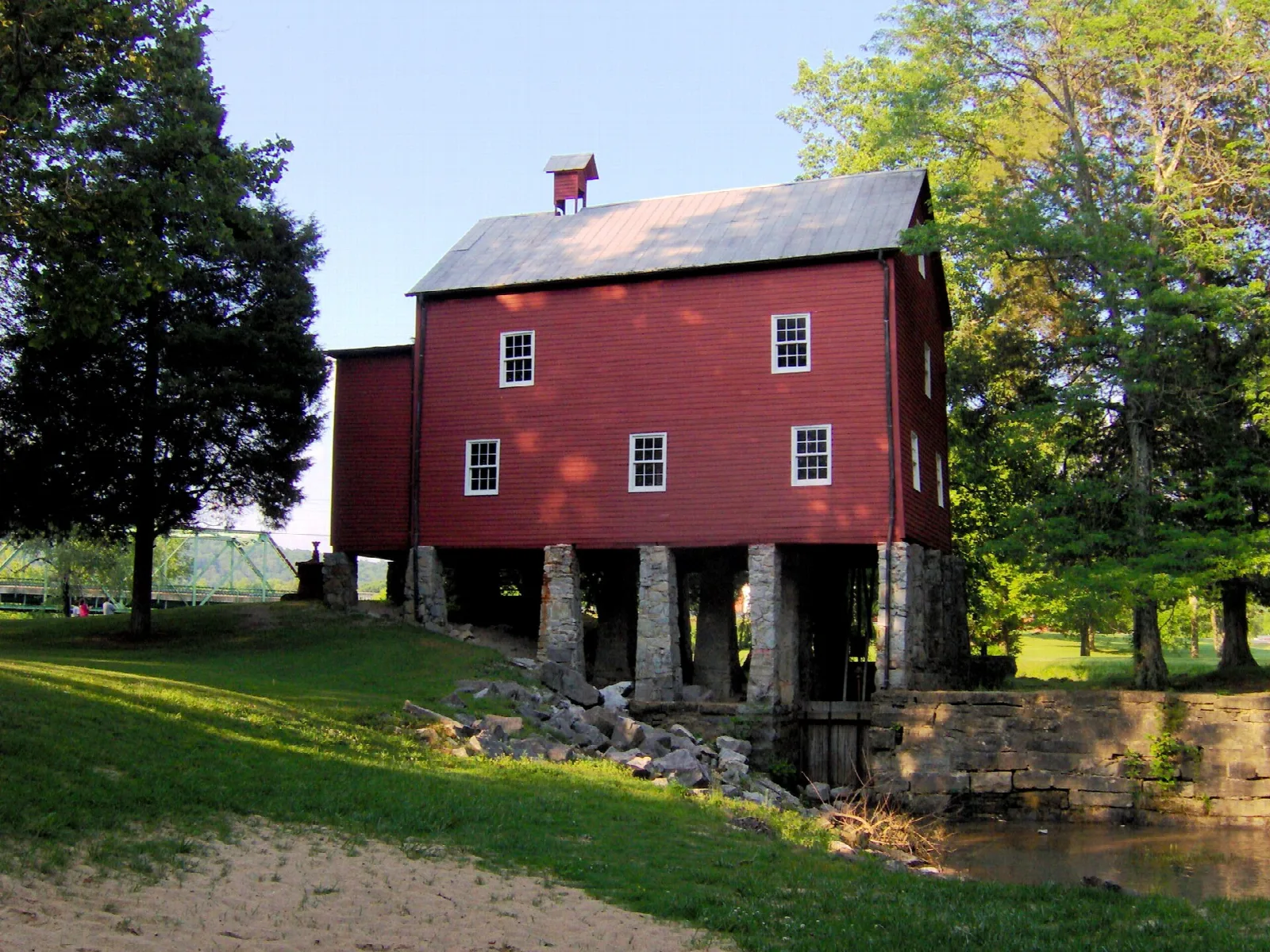 Red wooden gristmill on stone piers beside a green lawn