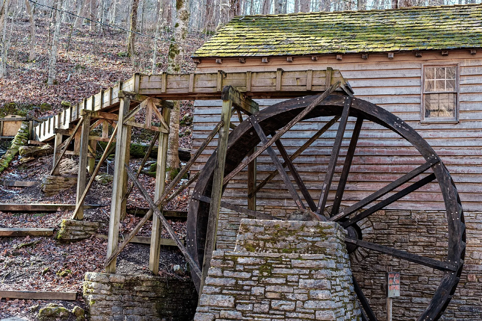 Wooden overshot water wheel and flume beside a stone and wood mill