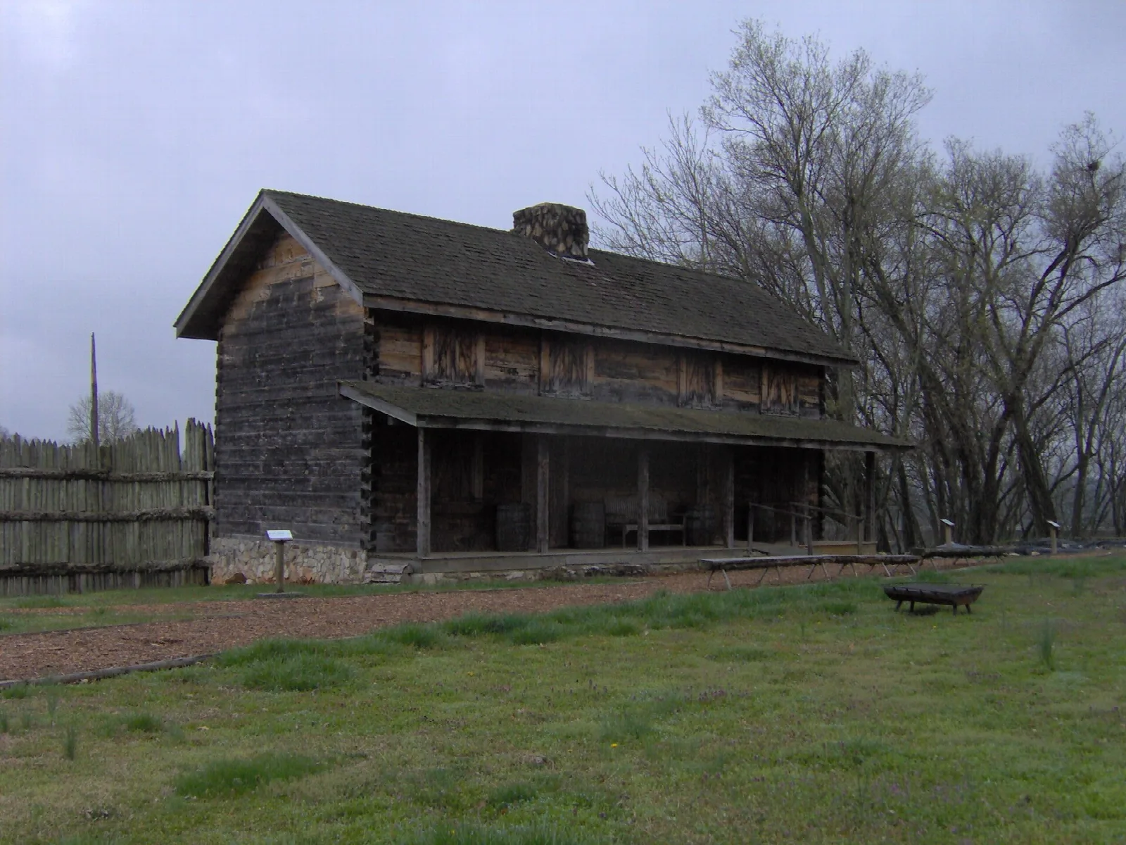 A log gatehouse building behind a wooden palisade under grey sky