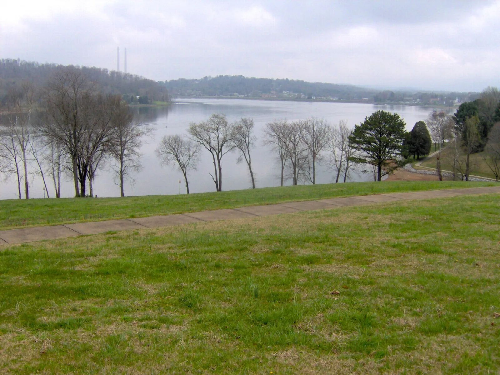 A wide river seen from a grassy shore with a path and trees