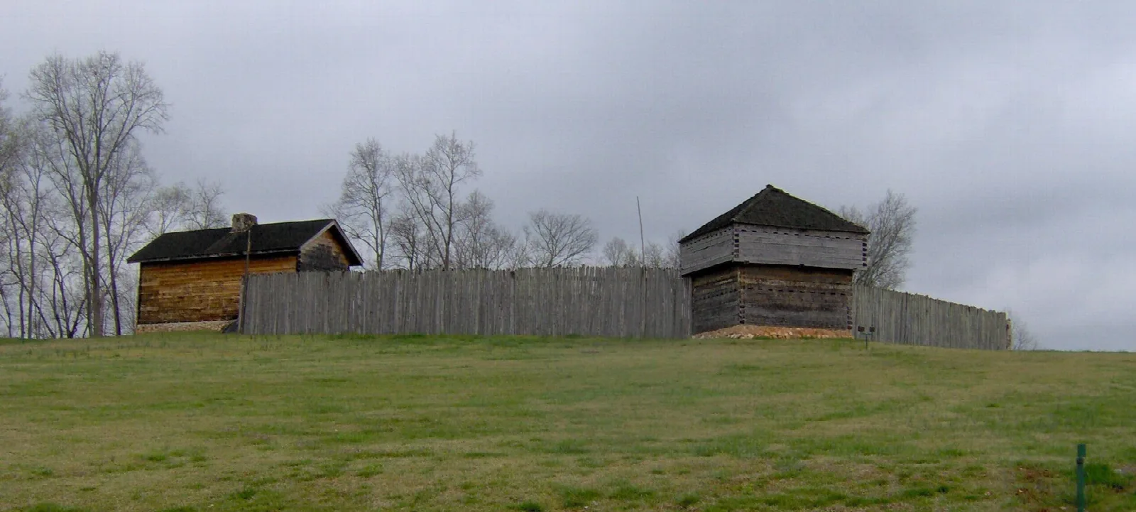 Reconstructed log blockhouses and a wooden palisade on a grassy hill